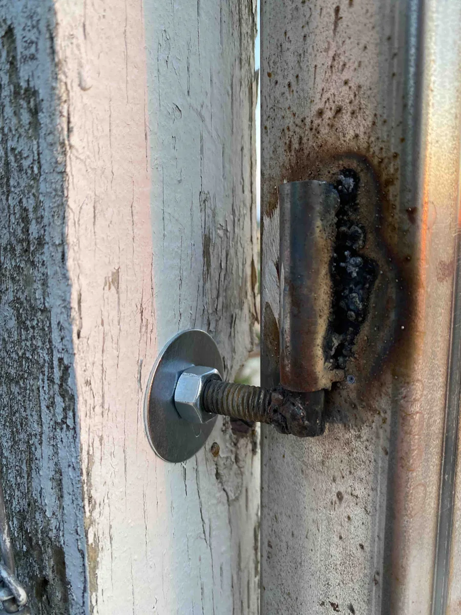 Homemade gate hinge with a threaded bolt and welded metal sleeve